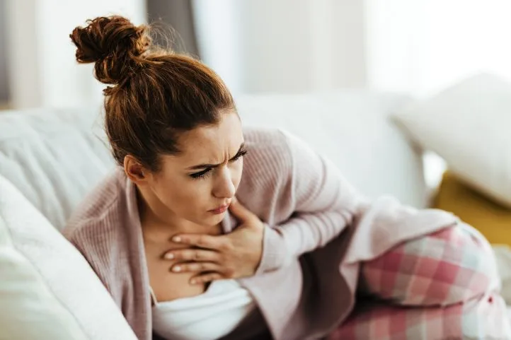 Distraught woman holding her chest pain while lying down sofa living room jpg