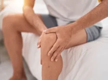 Young blond man suffering knee injury sitting bed bedroom jpg 215x161