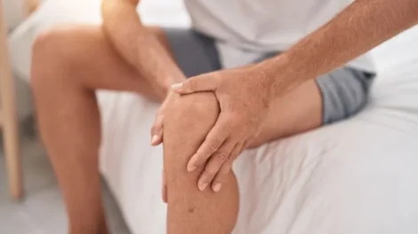 Young blond man suffering knee injury sitting bed bedroom jpg 470x264