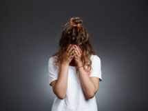 Young beautiful girl hiding face with hands grey wall 215x161