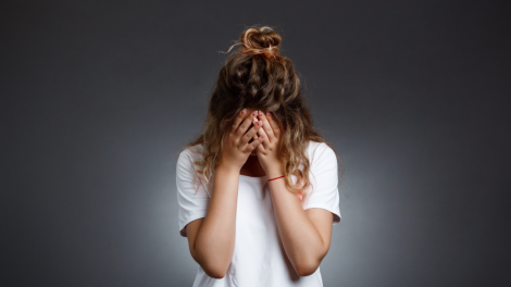 Young beautiful girl hiding face with hands grey wall 470x264