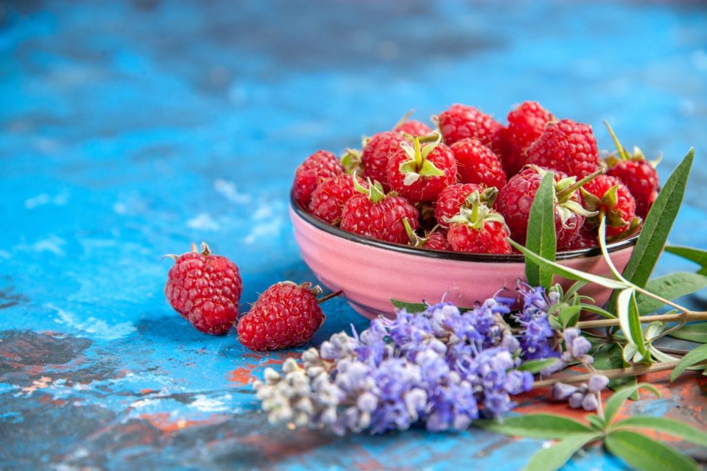 Front view raspberries bowl purple flowers blue table free place 1024x682