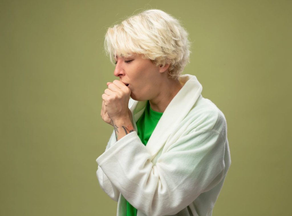 Sick unhealthy woman with short hair feeling unwell coughing standing light wall 1024x756