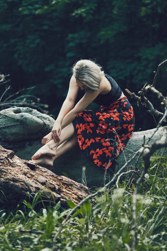 Vertical shot attractive blonde female with floral dress sitting tree log looking down 682x1024
