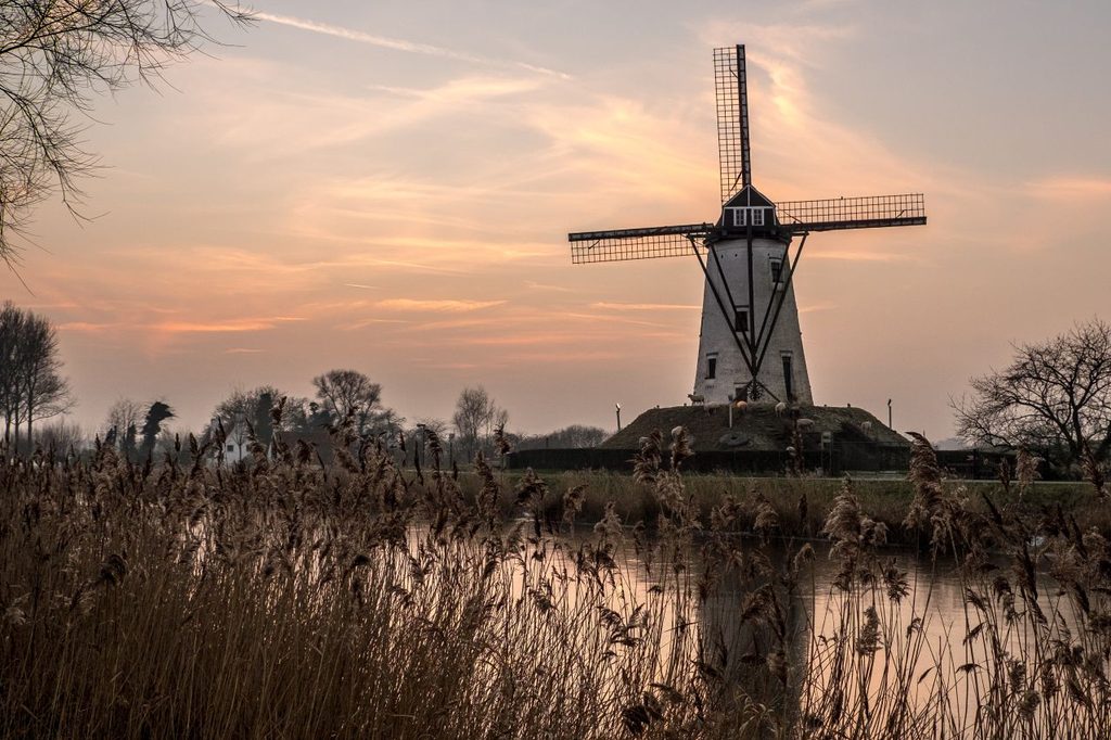White windmill near lake surrounded by grass beautiful sky 1024x682
