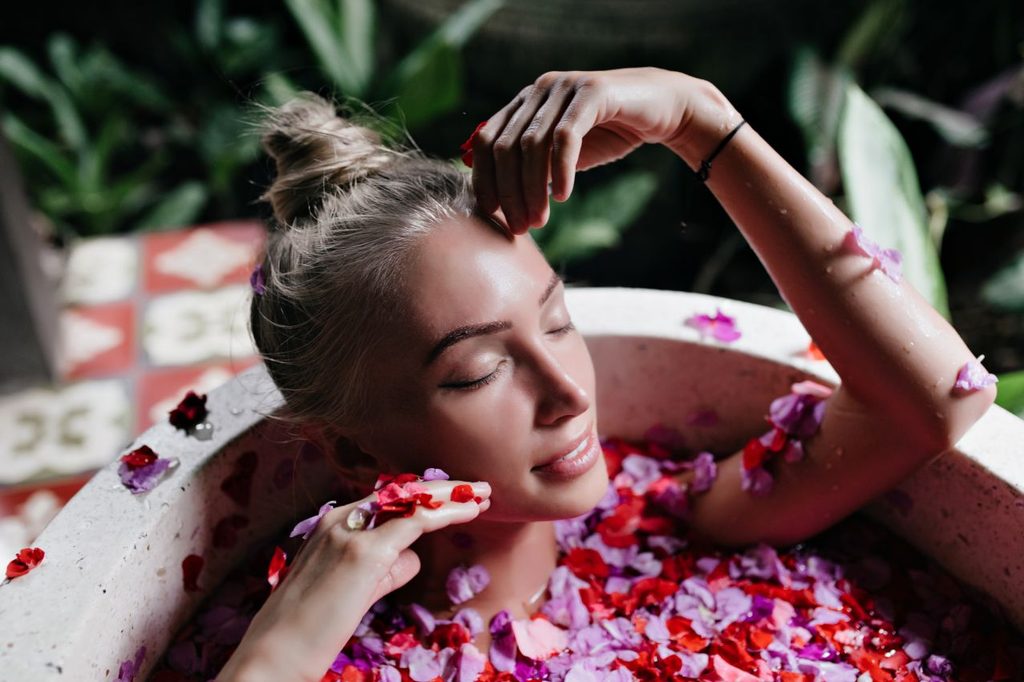 Close up photo attractive tanned woman chilling bath full rose petals indoor overhead shot refined blonde female model enjoying spa with gently smile 1024x682