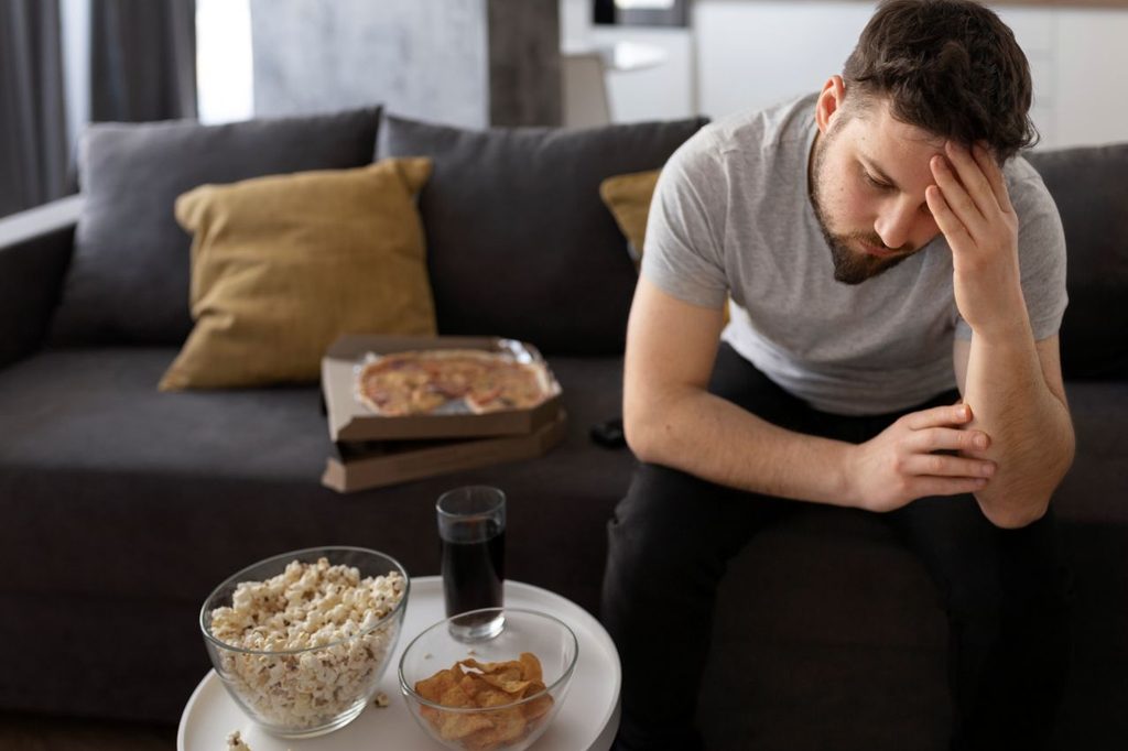 Young man tired sofa home sitting junk food 1024x682