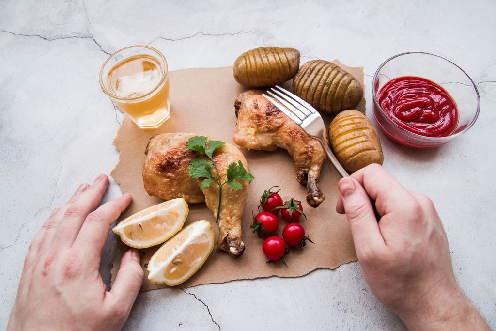 Person hand with fork against roasted chicken with potatoes beer 1024x683