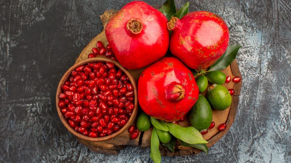 Top close up view pomegranates three pomegranates pomegranate seeds cutting board 990x556