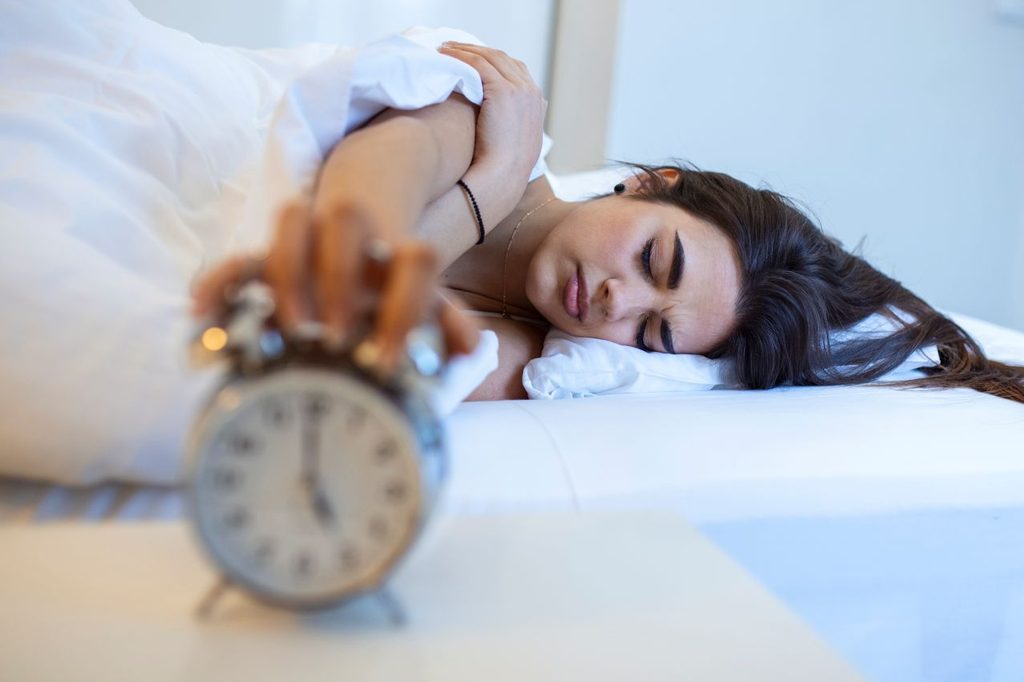 Woman lying bed turning off alarm clock morning 5am hand turns off alarm clock waking up morning girl turns off alarm clock waking up morning from call 1024x682